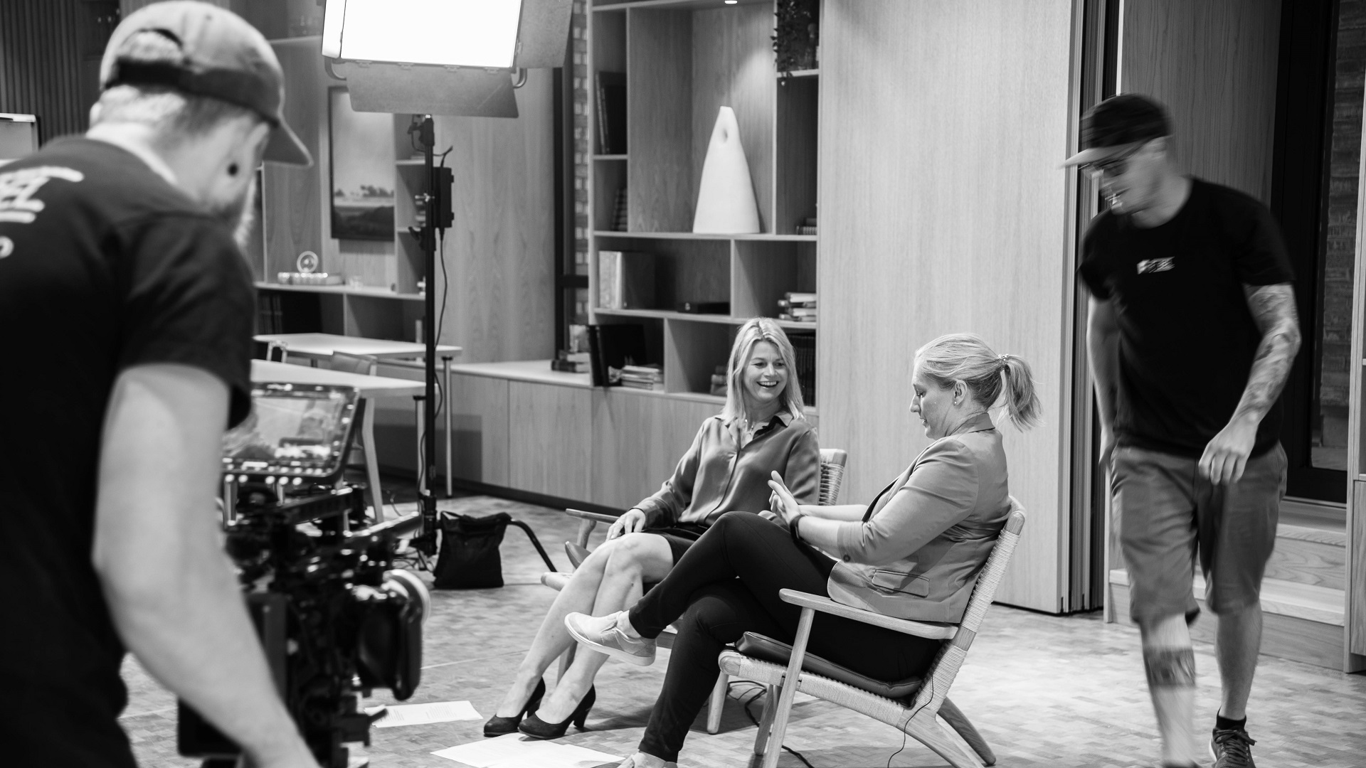 Two women talking, two men working in the back.